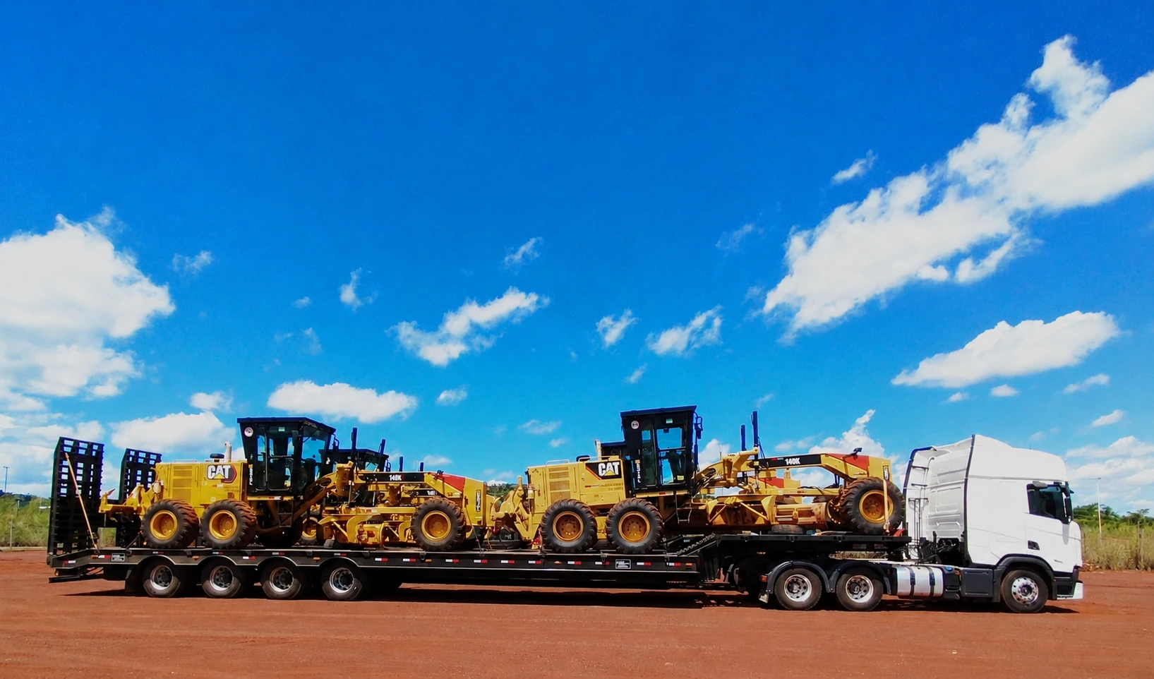 Carreta prancha transportando máquinas sob céu azul